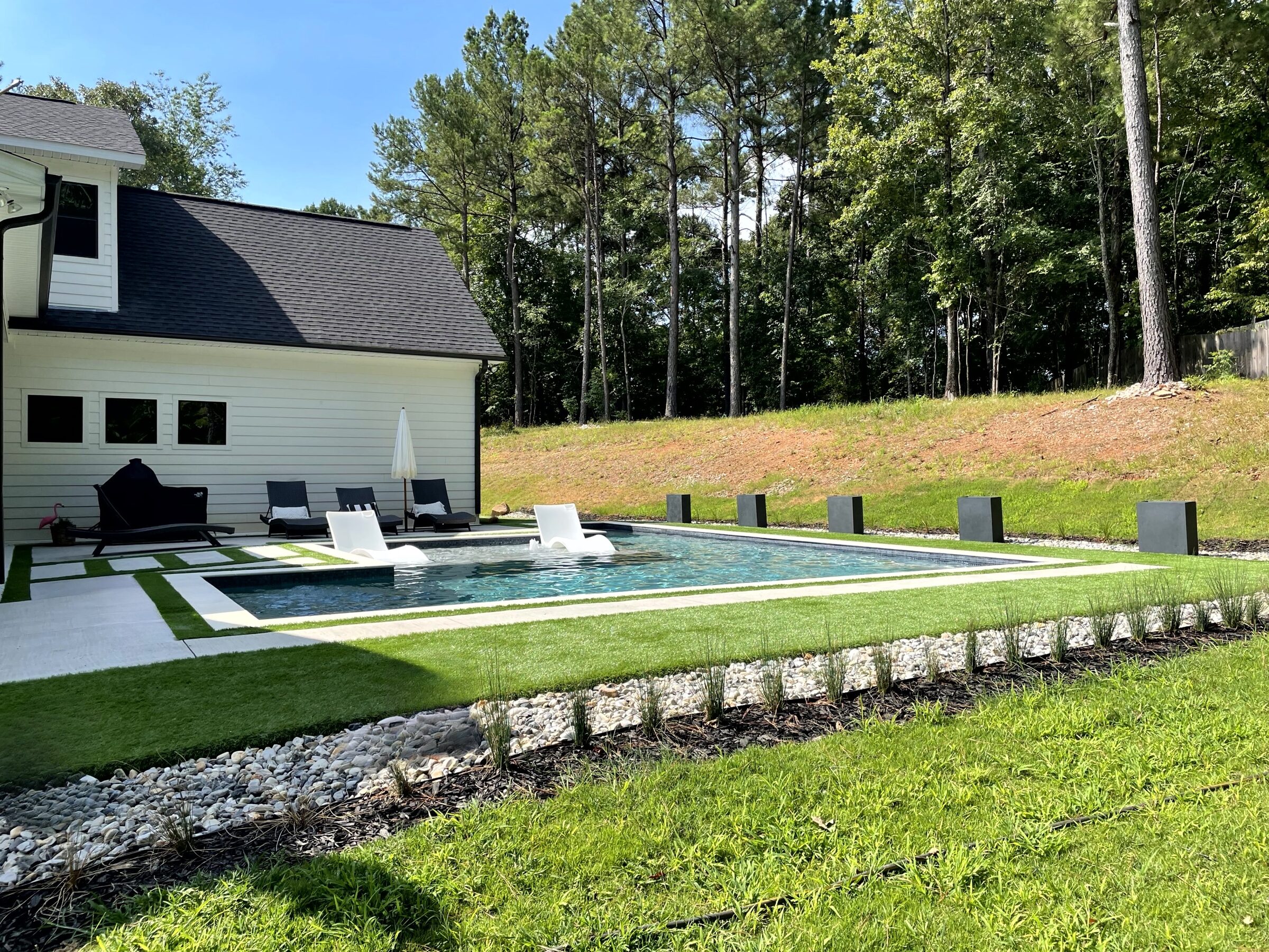 Pool wrapping the home — black mosaic waterline against limestone